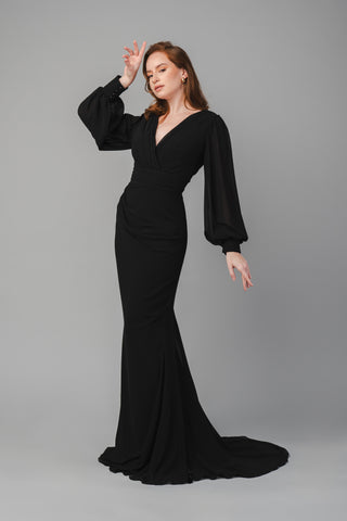 The Elea dresses Clara dress in black features a pleated V-neckline and is tailored around the waist. It is a fitted dress with a small train. The sleeves are balloon-styled, and the cuffs feature detailed buttons.