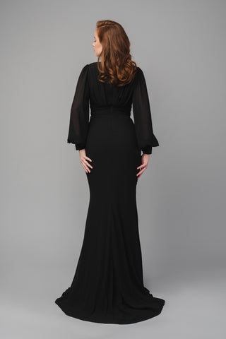 The Elea dresses Clara dress in black features a pleated V-neckline and is tailored around the waist. It is a fitted dress with a small train. The sleeves are balloon-styled, and the cuffs feature detailed buttons.