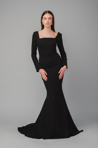 The Elea Dresses Louana dress in black is a fitted dress with long sleeves and a short train. The bodice is structured and features a square neckline.