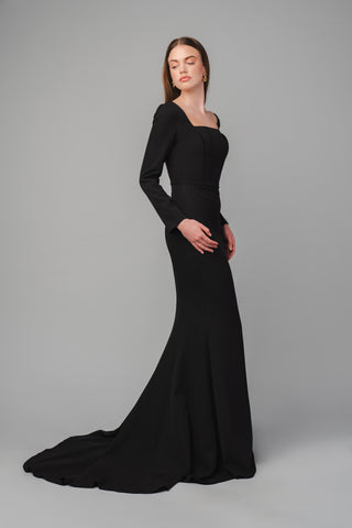 The Elea Dresses Louana dress in black is a fitted dress with long sleeves and a short train. The bodice is structured and features a square neckline.