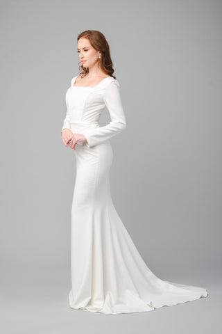 The Elea Dresses Louana dress in white is a fitted dress with long sleeves and a short train. The bodice is structured and features a square neckline.