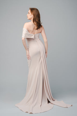 The Elea Dresses Quinn dress is strapless and features a beaded bust that extends over one shoulder. It is fitted, with a short train and an additional pleated train on the side.