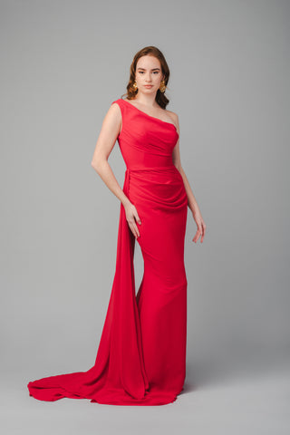 The Elea Dresses Selina dress in red is a one-shoulder fitted dress with a train. The top is pleated, and there is an additional pleated train on the side.