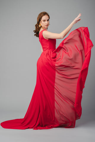 The Elea Dresses Selina dress in red is a one-shoulder fitted dress with a train. The top is pleated, and there is an additional pleated train on the side.